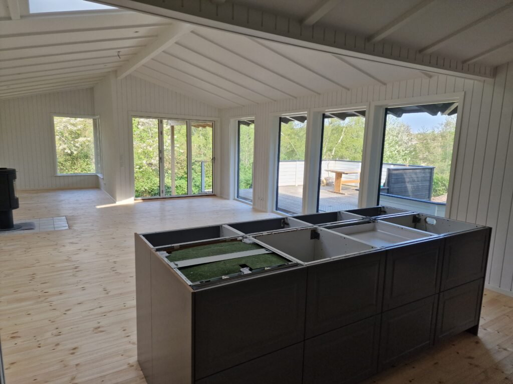 Lyst stue og køkken med store vinduer mod terrasse